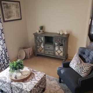 A cozy living room corner featuring a mirrored cabinet, an armchair with patterned cushions, and a decorated coffee table.