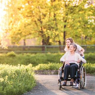A caregiver joyfully pushes a wheelchair through a sunlit path, highlighting the bond of support and friendship.
