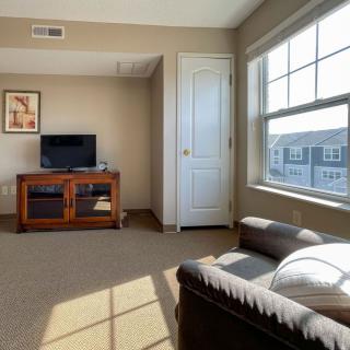 A cozy living room with a television, sofa, and large window letting in sunlight.