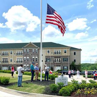 A group of people gather around a flagpole displaying the American flag in front of a large building.