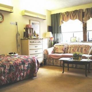 A cozy bedroom with a bed, sofa, and dresser in a warmly lit atmosphere.