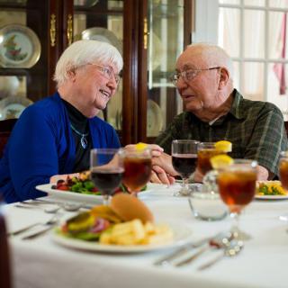 An elderly couple enjoying a meal together, sharing laughter and holding hands.