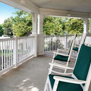 A peaceful porch with green-cushioned rocking chairs overlooking a sunny garden.