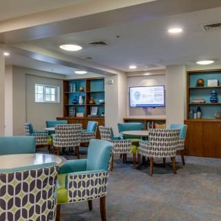 A cozy lounge area with patterned chairs and tables, featuring a television and bookshelves.