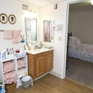 A bathroom interior with a sink, mirror, and neatly organized towels, leading into a bedroom.