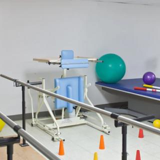 A physical therapy room with parallel bars and various rehabilitation equipment including exercise balls and cones.