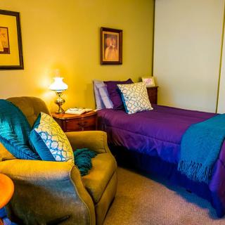 A cozy bedroom with a single bed, armchair, and warm lighting.