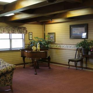 A cozy living room with traditional decor, featuring a grand piano, wooden beams, and plush carpeting.