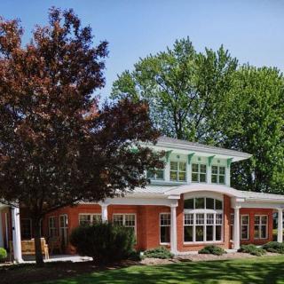 A two-story brick house with large windows surrounded by trees and a well-maintained lawn.