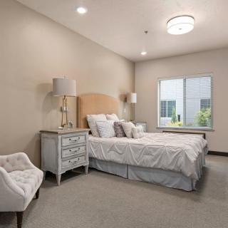 A cozy bedroom with a neatly made bed, bedside tables with lamps, and a window letting in natural light.