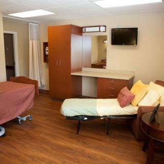 A well-appointed hospital room with a bed, couch, and television.
