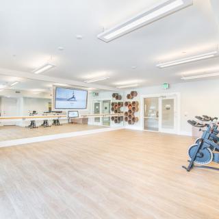 A bright fitness studio with a wooden floor, mirrors, and a stationary bike.