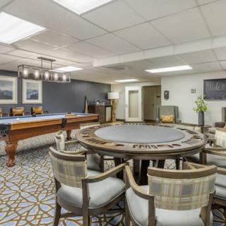 A spacious game room featuring a poker table and a pool table, with stylish chairs and decorative lighting.