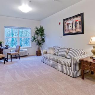A cozy living room with a striped sofa, desk area, and large window providing natural light.