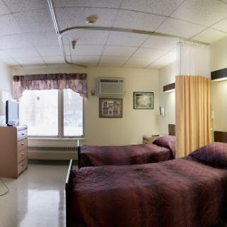 A well-furnished hospital room featuring two beds and a window with natural light.