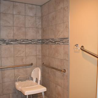 Accessible bathroom with a folding shower chair and grab bars.
