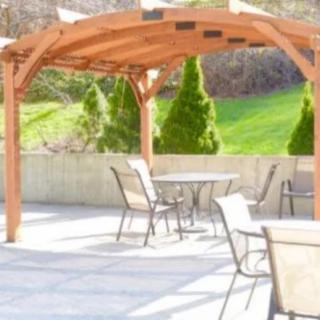 An outdoor patio featuring a wooden pergola, tables, and chairs overlooking a landscaped garden.