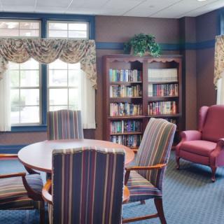 A cozy reading room with a round table, striped chairs, and a bookshelf by the window.