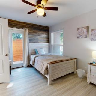 A cozy bedroom with a bed, wooden accents, and natural lighting from the windows.