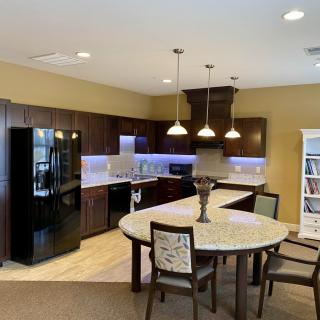 A modern kitchen with wood cabinets and a connected dining area, featuring contemporary lighting and appliances.