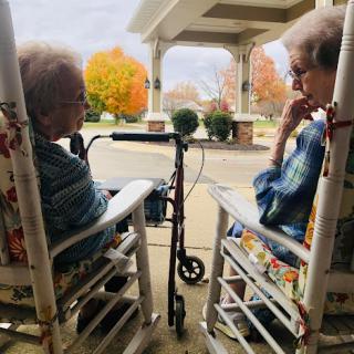 Two elderly women enjoying a peaceful moment together on a porch during autumn.