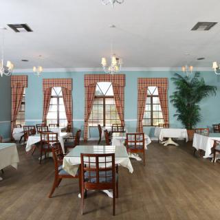 An elegant dining room with neatly arranged tables and chairs, featuring large windows with curtains and chandeliers for lighting.