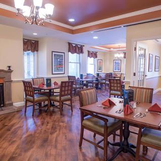 An elegant dining room with neatly arranged tables and chairs, featuring a chandelier and warm wooden flooring.