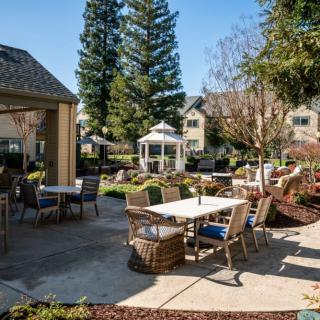 A sunny outdoor patio area with tables, chairs, and a gazebo surrounded by landscaped greenery.