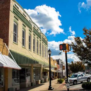 A quaint small-town street view with historic storefronts and a bright, cloudy sky.