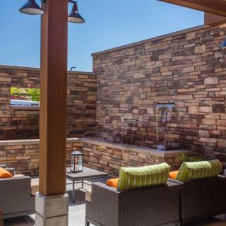 A cozy outdoor patio with cushioned seating and a stone wall under a clear blue sky.