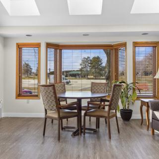 A cozy dining area with large windows and ample natural light, featuring wooden furniture and a plant for added decor.