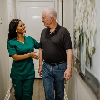 A nurse assists an elderly patient in a hallway, providing supportive care.