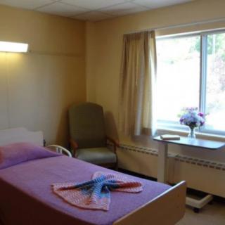 A hospital room with a bed, chair, and window overlooking greenery.