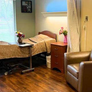 A cozy hospital room with a bed, chair, and side table decorated with flowers.