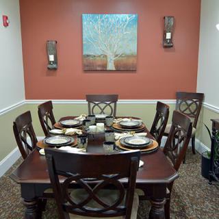 A neatly set dining table with six chairs in a warmly decorated room featuring wall art and candles.