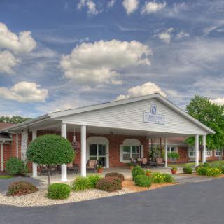 A welcoming entrance of a building surrounded by lush greenery and a dramatic sky.