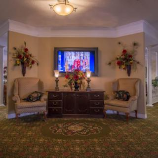 A traditional living room setup featuring a television, elegant chairs, and floral decorations.