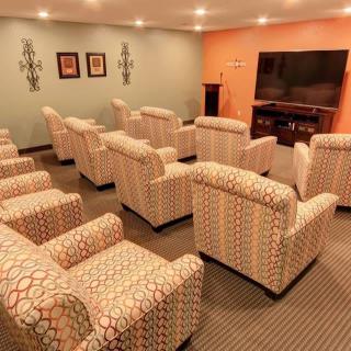 A cozy theater room with patterned armchairs facing a large television.