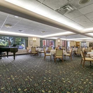 A spacious dining area with tables and chairs, featuring a grand piano near the windows.