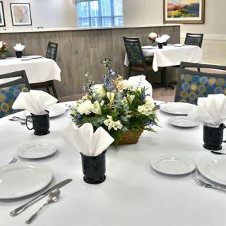 An elegantly set dining table with a floral centerpiece and neatly arranged white napkins.