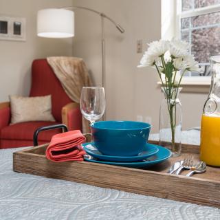 A cozy living room setting with a breakfast tray featuring blue dishware, orange juice, and flowers.