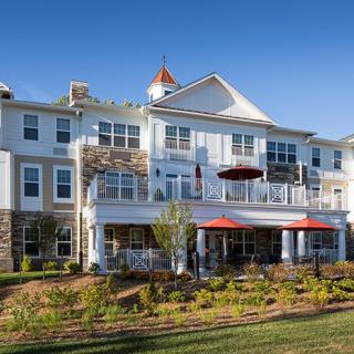 A large residential building with landscaped gardens and multiple windows under a clear blue sky.