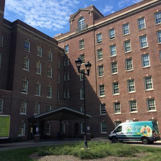 A view of a brick building with multiple windows and an entrance, accompanied by a delivery van.