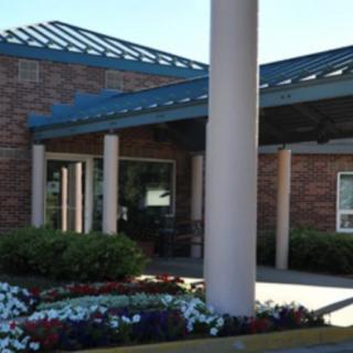 A brick building entrance with flower landscaping and a covered walkway.