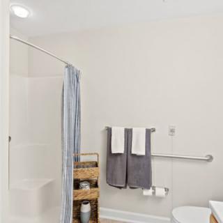 A minimalist bathroom with a shower, neatly arranged towels, and a storage shelf.