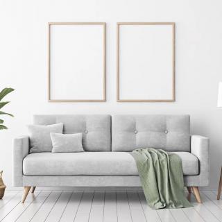 A minimalist living room featuring a grey sofa with a green throw blanket, accent pillow, and two blank frames on the wall.