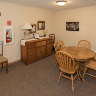 A cozy dining room with a wooden table and chairs, decorated with artwork and a sideboard with a lamp.