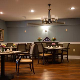 A cozy dining room with neatly arranged tables and chairs, featuring a chandelier and wooden flooring.