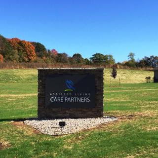 A stone sign stands in a grassy field with trees in the background under a clear blue sky.