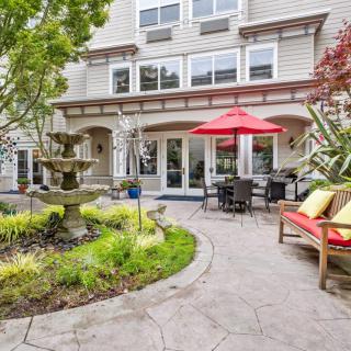A charming outdoor patio with a fountain, surrounded by lush greenery and comfortable seating under a red umbrella.